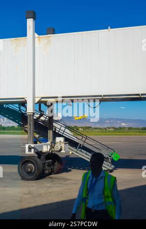 Sonnenaufgangsflugzeuge fliegen im Hintergrund, eingerahmt von einem leeren Jetway, der darauf wartet, dass das nächste Flugzeug am Flughafen Port-Au-Prince ankommt Stockfoto