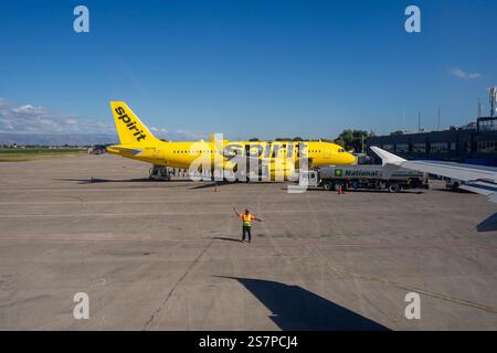 Weitwinkelansicht einer Asphaltfläche, auf der Spirit Airlines Passagiere aussteigen, während ein Luftmarshaller ein anderes Flugzeug aus dem Rahmen lenkt Stockfoto
