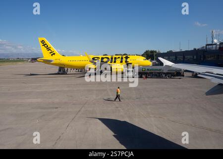 Weitwinkelansicht einer Asphaltfläche, auf der Spirit Airlines Passagiere aussteigen, während ein Luftmarshaller ein anderes Flugzeug aus dem Rahmen lenkt Stockfoto