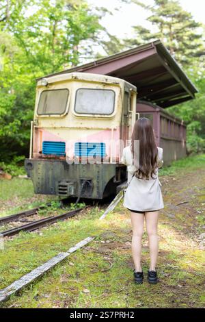 Eine Japanerin im Alter von 20 Jahren in weißer Kleidung verbringt ihre Zeit in einem ungenutzten Zug in einem Park voller Natur in Japan. Stockfoto