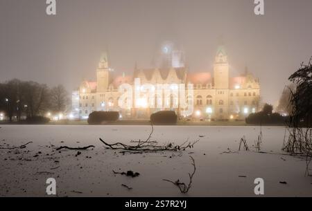 Hannover, Deutschland. Januar 2025. Das neue Rathaus wird am frühen Morgen bei Nebel und unter dem Gefrierpunkt beleuchtet, während eine dünne Eisschicht den Maschteich im Maschteich bedeckt. Quelle: Julian Stratenschulte/dpa/Alamy Live News Stockfoto