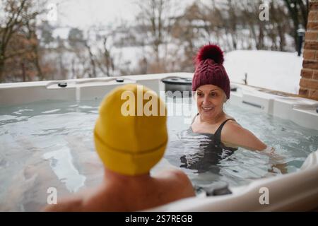 Seniorenpaar baden im Wannen-Whirlpool an kalten Wintertagen. Romantischer Wellness-Kurzurlaub mit Spa am Valentinstag-Wochenende. Stockfoto