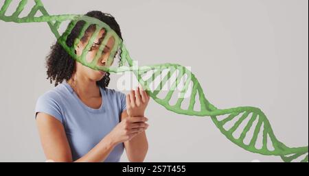 Bild eines dna-Strangs über der afroamerikanischen Frau, die ihr Handgelenk hält Stockfoto