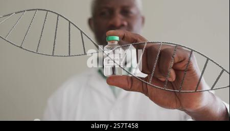 Bild des dna-Strangs über dem männlichen afroamerikanischen Arzt, der das Fläschchen hält Stockfoto