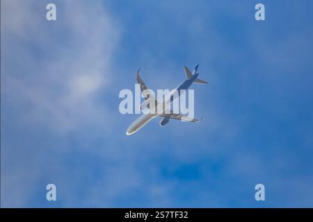 Passagierflugzeug, das vor blauem Himmel mit Wolken vorbeifliegt. Nahaufnahme, Ansicht von unten. Stockfoto