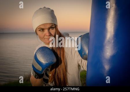 Junge Frau posiert mit Boxhandschuhen und Boxsack Stockfoto