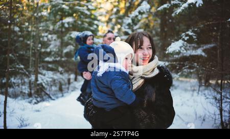 Glückliche Familie, die einen sonnigen Winterspaziergang durch einen verschneiten Wald genießt und freudige Erinnerungen schafft, während sie sich in der Schönheit der Natur verbindet Stockfoto