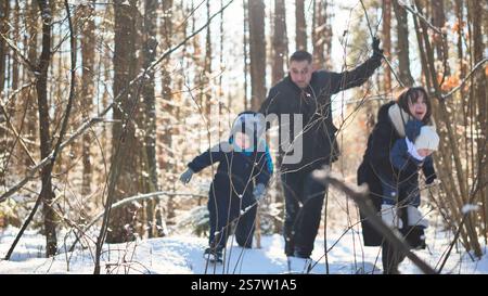 Die Familie spielt fröhlich im verschneiten Winterwald, lacht und rennt durch die helle, frostige Waldlandschaft und teilt fröhliche Momente im Freien Stockfoto