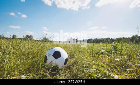 Klassischer Fußball aus Leder, der an einem sonnigen Sommertag im Gras liegt und die Schüler im Hintergrund spielen Stockfoto