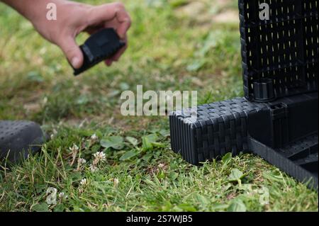 Nahaufnahme einer Hand, die einen schwarzen Kunststofffuß an einem Gartenmöbel befestigt. Die Möbel haben ein gewebtes Design und werden montiert Stockfoto