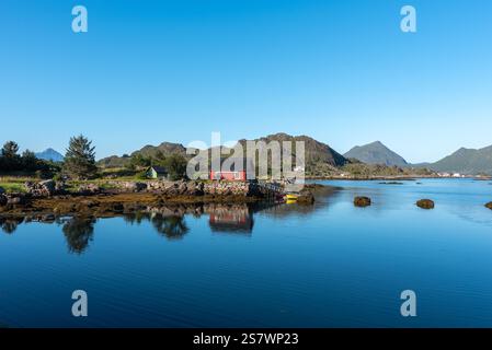 Blick auf die Landschaft der Skotnesosen Bucht mit traditionellem rotem Fischerhaus, genannt rorbu, Ballstad, Lofoten, Norwegen, Europa Stockfoto