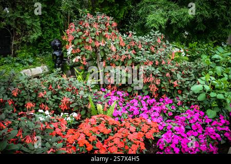 Ein Garten mit einer Statue einer Frau und einer Bank. Der Garten ist voller Blumen und Pflanzen Stockfoto
