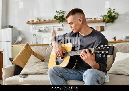 Ein junger Mann in legeren Kleidern spielt zu Hause Gitarre, umgeben von schlichtem, aber stilvollem Dekor. Stockfoto