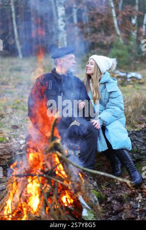 Verliebte Paare tragen Winterkleidung und sitzen am Feuer im Wald Stockfoto