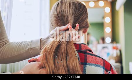 Professioneller Friseur mit schlankem Pferdeschwanz für blonde Kunden in einem modernen, gut beleuchteten Salon mit reflektierenden Oberflächen Stockfoto