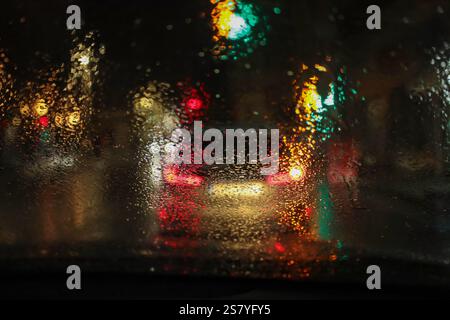 Regnerische nächtliche Atmosphäre durch die Windschutzscheibe eines Autos, mit starken Regentropfen auf dem Glas. Stockfoto
