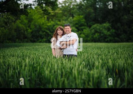 Glückliche Eltern halten ihr neugeborenes Baby in einem grünen Weizenfeld und genießen einen friedlichen gemeinsamen Moment inmitten der Natur Stockfoto