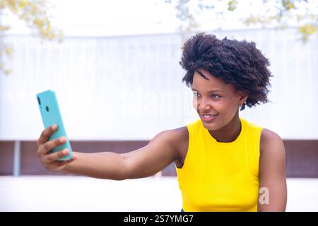 Aufgeregt afroamerikanische junge Frau, die draußen ein Selfie mit einem Smartphone macht Stockfoto