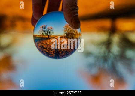 Eine Hand, die eine Glaskugel hält, mit einer Reflexion von Bäumen und Wasser Stockfoto