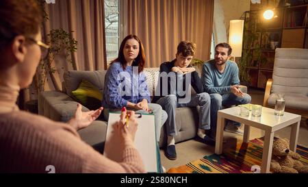 Frau, Psychologin redet lebhaft mit einer dreiköpfigen Familie, einschließlich Eltern und Teenager, über Kommunikationsprobleme Stockfoto