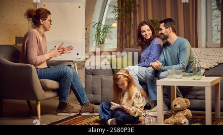 Psychologin regt und diskutiert Probleme der Familie. Eltern sitzen auf der Couch mit positivem Ausdruck, ihre Tochter sitzt auf dem Boden und Stockfoto