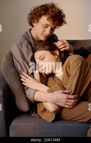 Vertikale Aufnahme eines jungen Paares, das auf der Couch liegt, Mann, der seine Frau umarmt und sie unterstützt Stockfoto