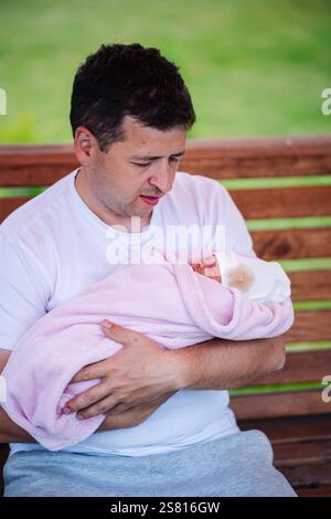 Vater, der sein schlafendes, neugeborenes Mädchen in eine rosa Decke einhüllt, genießt einen friedlichen Moment zusammen Stockfoto
