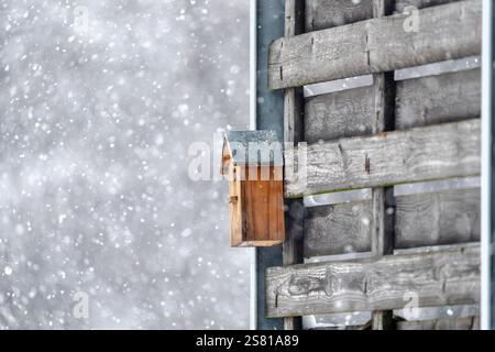 Ein Vogelhaus sitzt auf einem Holzzaun im Schnee. Das Vogelhaus ist klein und braun, und es ist von viel Schnee umgeben. Das Bild hat ein Friedensfu Stockfoto