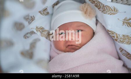 Schlafende Neugeborene mit weißer Mütze, eingebettet in rosa Decke in goldener gefiederter Wiege, weich und friedlich Stockfoto