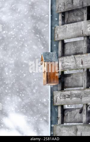Ein Vogelhaus sitzt auf einem Holzzaun im Schnee. Das Vogelhaus ist klein und braun, und es ist von viel Schnee umgeben. Das Bild hat ein Friedensfu Stockfoto