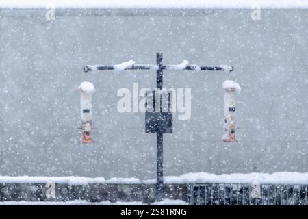 Zwei Vogelfütter sind mit Schnee bedeckt. Der Schnee fällt auf die Zuführungen und den Boden Stockfoto
