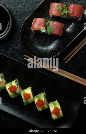 Eine elegante Sushi-Platte mit verschiedenen Brötchen auf schwarzen Tellern mit Beilagen und Stäbchen neben einer Sojasauce-Schüssel. Stockfoto