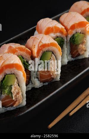 Nahaufnahme von Sushi-Lachsrollen auf einem schwarzen Teller mit Essstäbchen Stockfoto