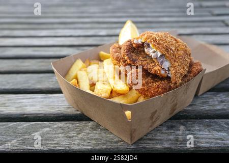 Fish and Chips in einem Karton auf einem verwitterten Holzsteg im Hafen, traditioneller Snack mit Meeresfrüchten an der Küste, Kopierraum, Blick von oben, se Stockfoto