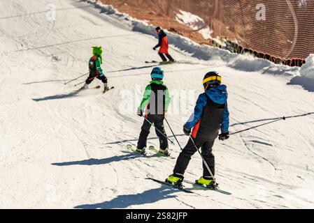 Gruppe von Menschen, die an einem sonnigen Wintertag in den Bergen Ski fahren. Skiunterricht mit ortskundigen Lehrern. Kinder lernen Skifahren mit einem Lehrer. Kinder Stockfoto