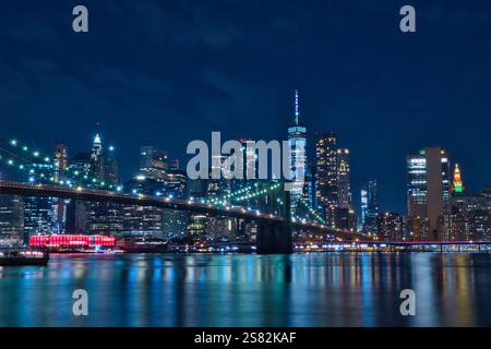 Nächtlicher Blick auf die Brooklyn Bridge und die Skyline von Lower Manhattan in New York City. Die ikonische Brücke wird mit leuchtenden Lichtern beleuchtet, wodurch ein s entsteht Stockfoto