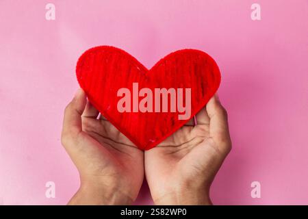 Nahaufnahme Herz in der Hand auf weichem rosa Hintergrund. Valentinstag Stockfoto