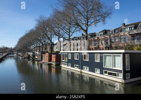Hausboote in Utrecht an einem sonnigen Tag mit blauem Himmel und Bäumen und Backsteinhäusern im Hintergrund, Brücke Stockfoto