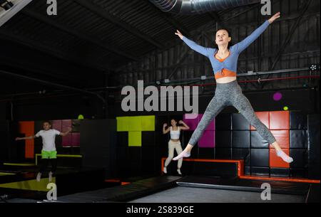 Glückliche Frau mittleren Alters, die auf Trampolinen in einem Sporthalle trampoliniert und springt, Workout und modernes Unterhaltungskonzept Stockfoto