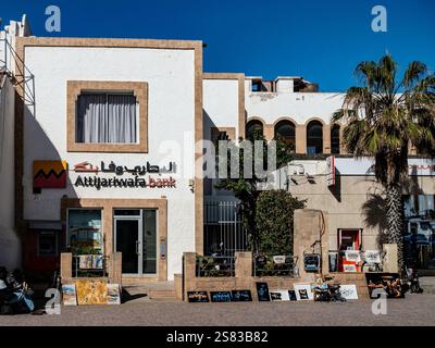 Das Gebäude zeigt ein einzigartiges Design der Attijariwafa Bank in Essaouira, Marokko, während lokale Künstler ihre Kunstwerke auf der Straße präsentieren. Stockfoto