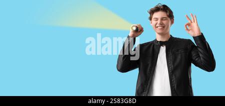Junger Mann mit Taschenlampe, die OK-Geste auf blauem Hintergrund mit Platz für Text zeigt Stockfoto