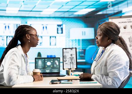 Afrikanisch-amerikanische Ärztin diskutiert mit einem Mädchen über gesundheitliche Bedenken und nutzt medizinische Daten und technische Geräte, um die Behandlung und Prävention zu verbessern. Klinische Untersuchung. Stockfoto