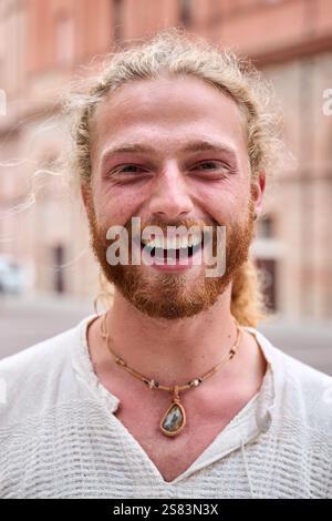 Porträt eines attraktiven, lächelnden jungen Mannes, der im Park in die Kamera schaut. Ein hübsches, weißes männliches Modell. Stockfoto