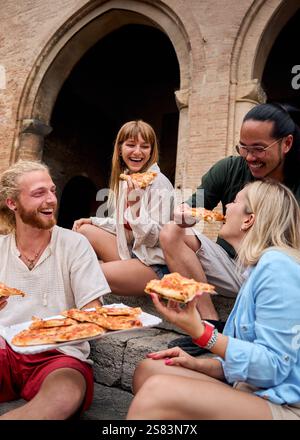 Lustige Gruppe junger Leute und sie haben Spaß beim Pizza essen in der touristischen Stadt Stockfoto