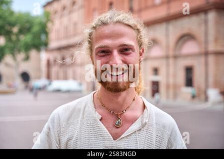 Porträt eines attraktiven, lächelnden jungen Mannes, der im Park in die Kamera schaut. Ein hübsches, weißes männliches Modell. Stockfoto
