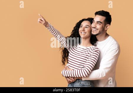 Fröhliches Junges Arabisches Paar, Das Mit Dem Finger Auf Copy Space Zeigt Stockfoto