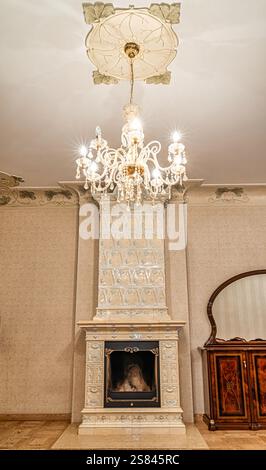 Ein elegantes Zimmer mit Keramikkamin, Kristallleuchter, Blumendeckenmedaillon, poliertem Holzschrank und Parkettboden. Stockfoto
