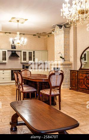 Innenblick auf einen Essbereich mit Holztisch, Vintage-Sideboard, floralem Kachelofen, modernen Küchengeräten und Parkettboden. Stockfoto