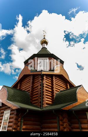 Eine hölzerne Kirche mit einem grünen Schindeldach und einer goldenen Kuppel, die mit einem Kreuz gekrönt ist, vor einem hellblauen Himmel mit verstreuten weißen Wolken. Stockfoto