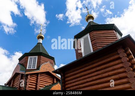 Zwei hölzerne Kirchtürme mit grünen Dächern und goldenen Kuppeln mit orthodoxen Kreuzen vor einem hellblauen Himmel mit verstreuten Wolken. Stockfoto